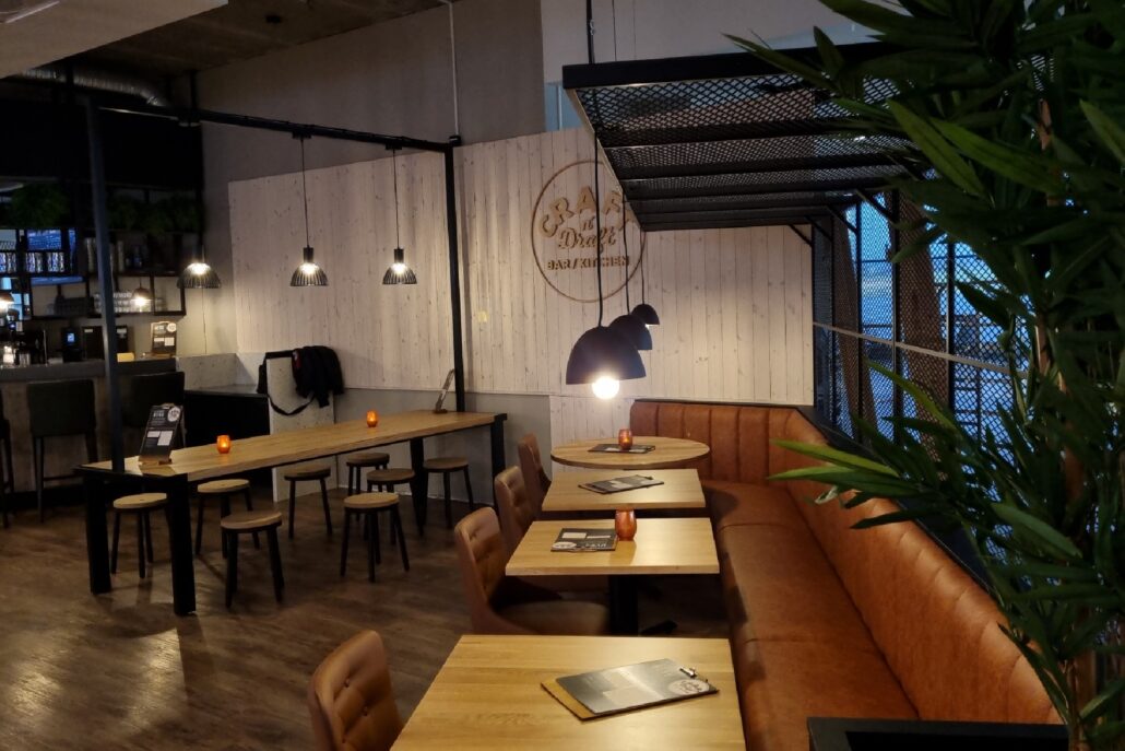 Sitteområde med brune skinnbenker, trebord og moderne pendellamper hos Craft’n Draft.