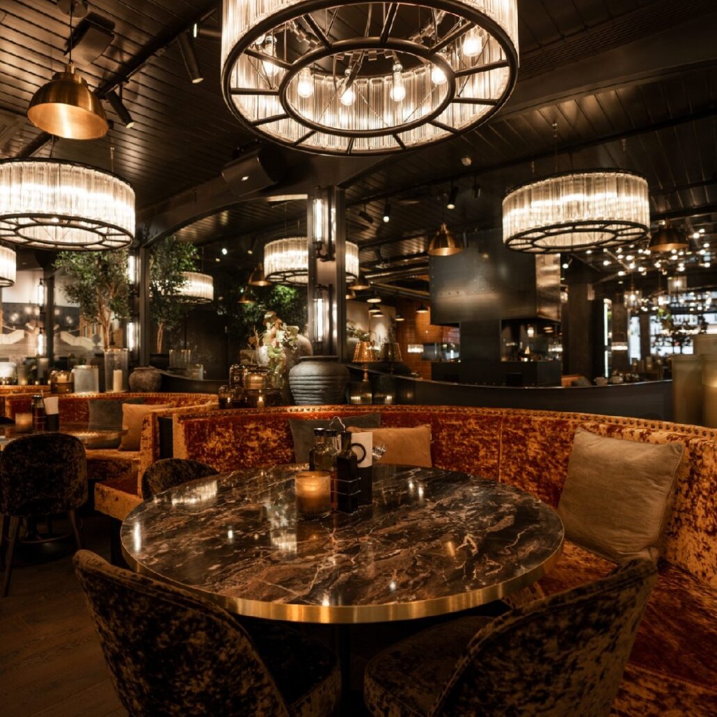 Restaurantinteriør på Olivia Kluuvi i Finland med runde marmorbord, velursofaer, store lysekroner og stemningsfull belysning.