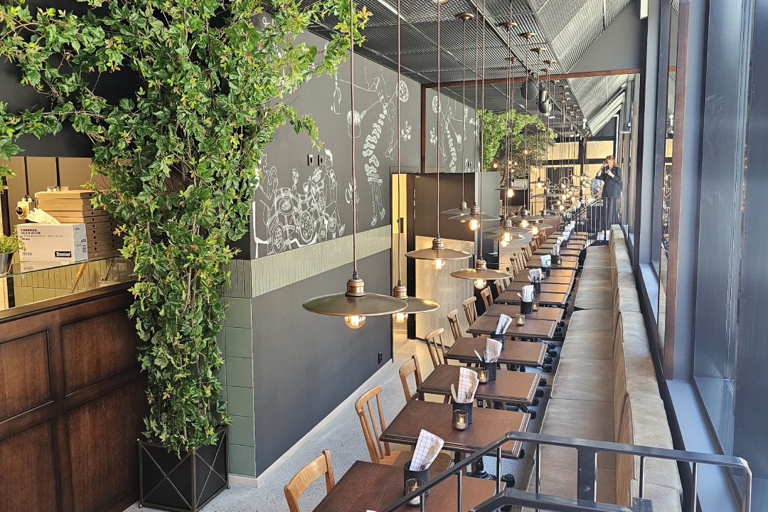 CiCi Osteria med lang rekke bord langs vinduene, hengelamper med industripreg, grønn dekor og veggkunst med italienske motiver.
