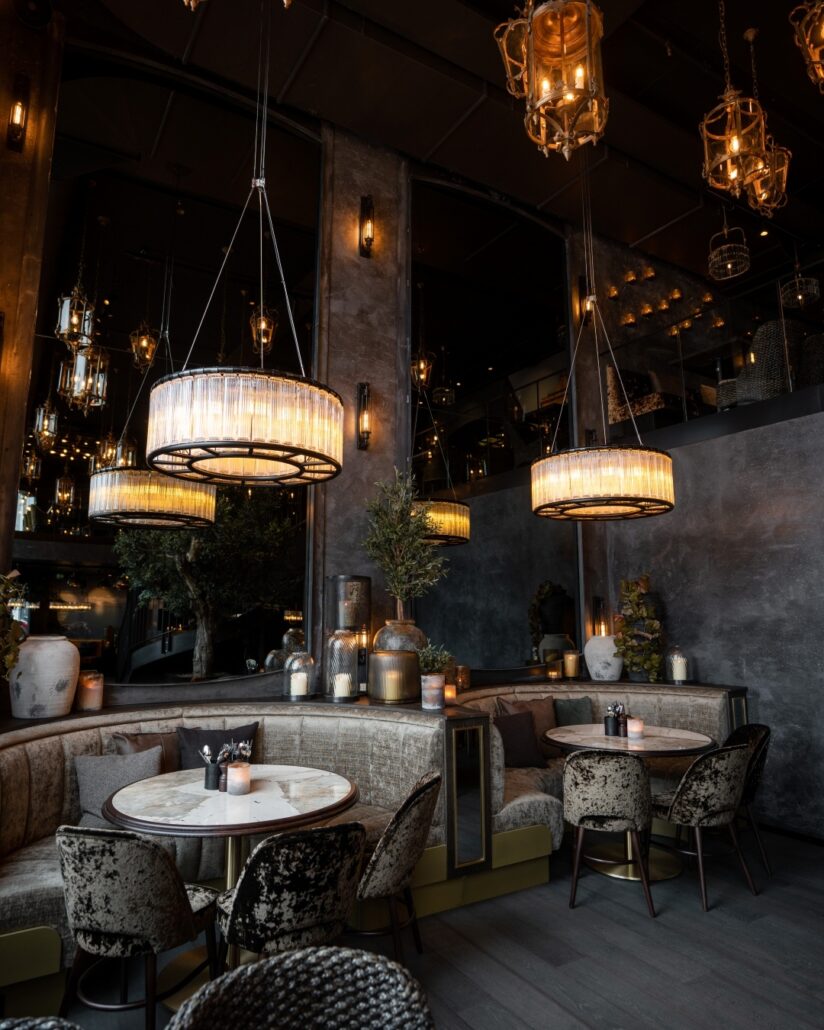 Restaurantinteriør på Olivia Vågen med runde marmorbord, velurseter og store hengelamper som skaper en stemningsfull atmosfære.